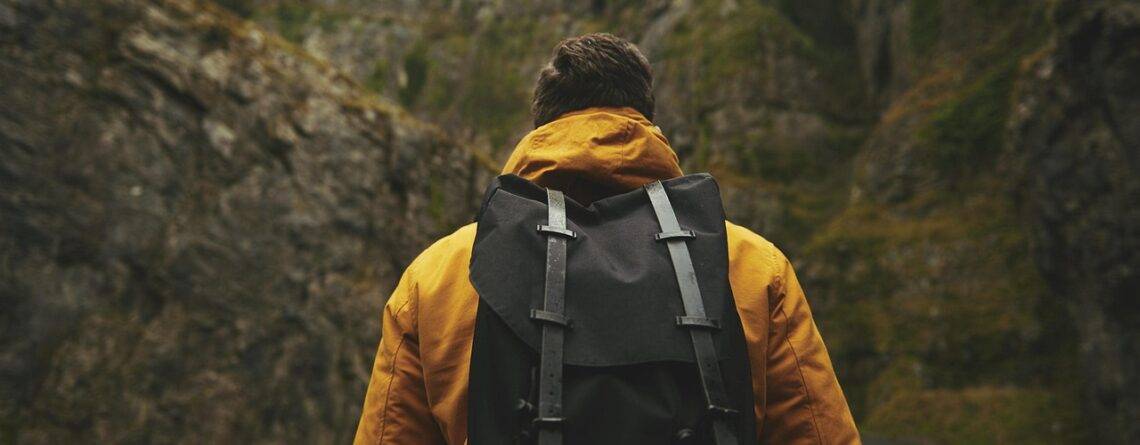 Digital nomad wearing a yellow jacket and a travel backpack walking through a mountain pass