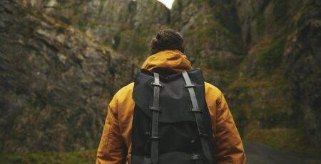 Digital nomad wearing a yellow jacket and a travel backpack walking through a mountain pass