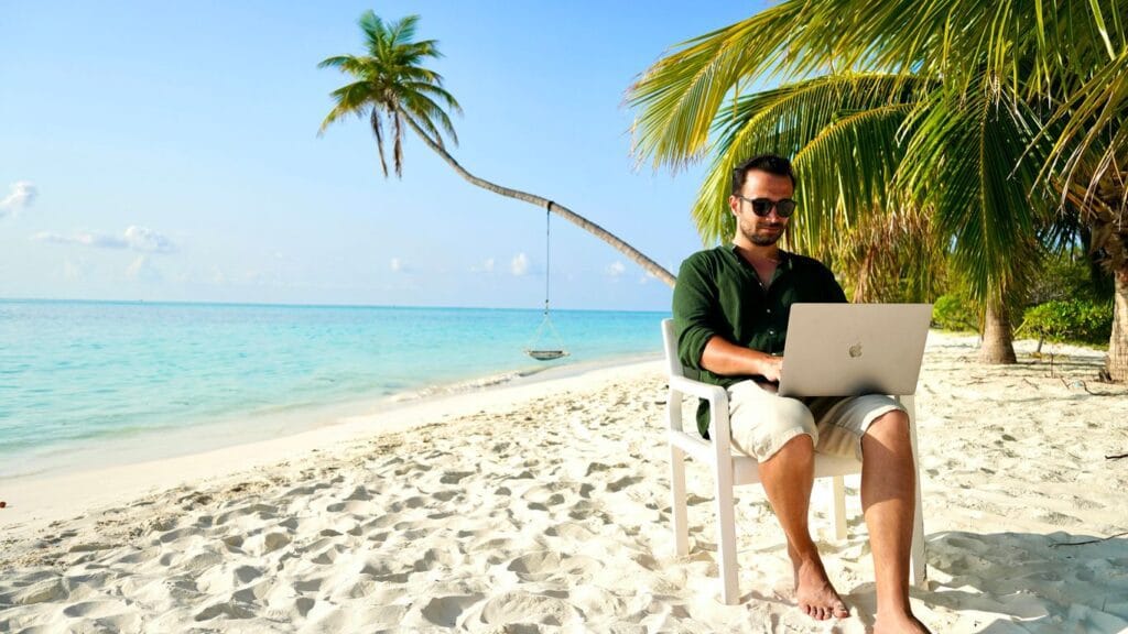 a man sitting in a chair on a beach using a laptop