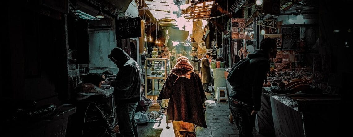 Traditional market street in Morocco with locals walking through a narrow souk, representing everyday life and travel safety in Morocco